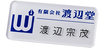 ロゴマーク等を透明プレートの裏側からシルク印刷し､後から名前をプレートの表面に彫刻した名札（正面から見た画像）